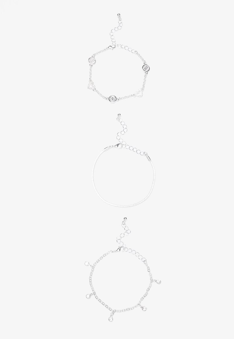 Tre bracciali d'argento: una catena con accenti circolari, un design in filo semplice e una catena con gioielli trasparenti pendenti.