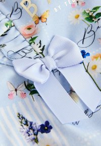 Tessuto azzurro chiaro con stampa floreale e farfalle, caratterizzato da un nastro azzurro pallido testurizzato annodato a fiocco.