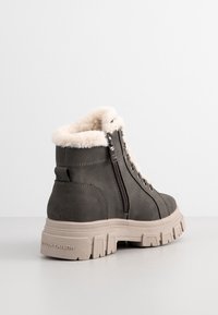 Botte d'hiver gris foncé avec semelle épaisse beige, fermeture éclair latérale, lacets et doublure en fourrure beige autour de la cheville.