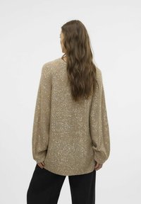 Langærmet, oversized sweater i beige med metalliske perler. Har en rund kant og løs pasform, parret med sorte bukser.