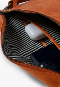 Braune Lederinnentasche mit gestreiftem Stofffutter. Enthält weiße Ohrhörer und ein schwarzes Smartphone. Mit Reißverschluss und orangefarbenen Akzenten.