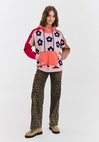 Farebná mikina s ružovým základom, námorníckymi kvetmi a koralovou vreckom. V kombinácii so vzorovanými nohavicami s leopardím potlačou a svetložltými šnurovacími čižmami.