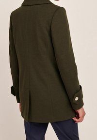 Olijfgroen wolmixjas met een enkele rugventilatie, notched revers en een bijbutton detail op de manchetten. Textuurstof met gestructureerde silhouet.