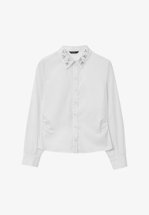 Camicia bianca a maniche lunghe con bottoni e colletto a punta decorato con piccole applicazioni di perline argentate.