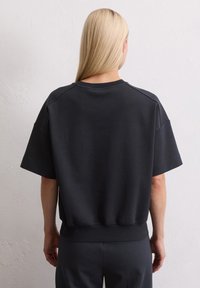 Zwarte cropped sweatshirt met brede korte mouwen en geribde zoom. Glad, zacht textuur en minimale ontwerpelementen zichtbaar.