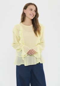 Helle gelbe Bluse aus transparenter Stoff, mit Rüschendetails entlang der Vorderseite und Ärmel, locker sitzend und mit einem schwingenden Design.