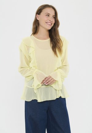 Blusa amarilla clara hecha de tela transparente, con acentos de volantes en el frente y las mangas, de corte holgado y diseño fluido.