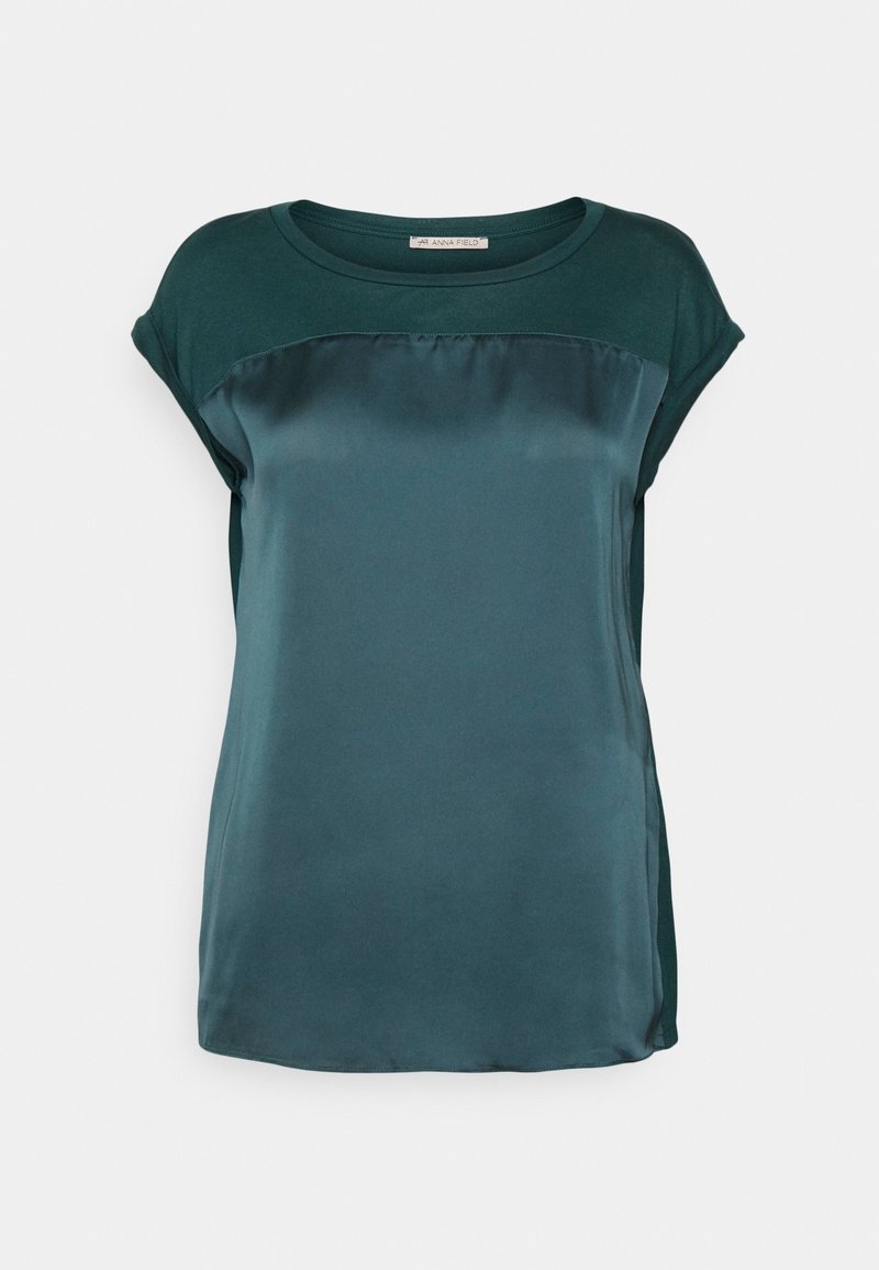 Haut teal à manches courtes avec un panneau avant en satin, en tissu doux, col rond et coupe décontractée avec fentes latérales.