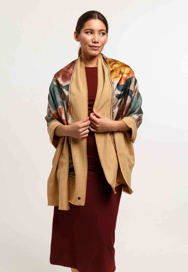 Multicolor floral shawl with a tan, fringe-trimmed edge; soft texture; draped over a maroon dress; open front design.
