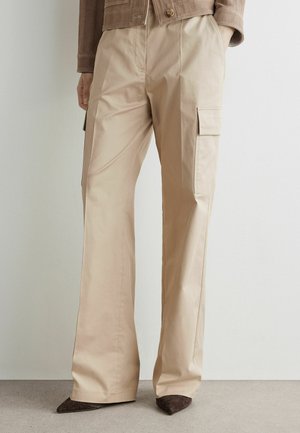 Pantalon cargo beige à jambes larges avec poches à rabat latérales, porté avec des chaussures marron à bout pointu et une veste courte.