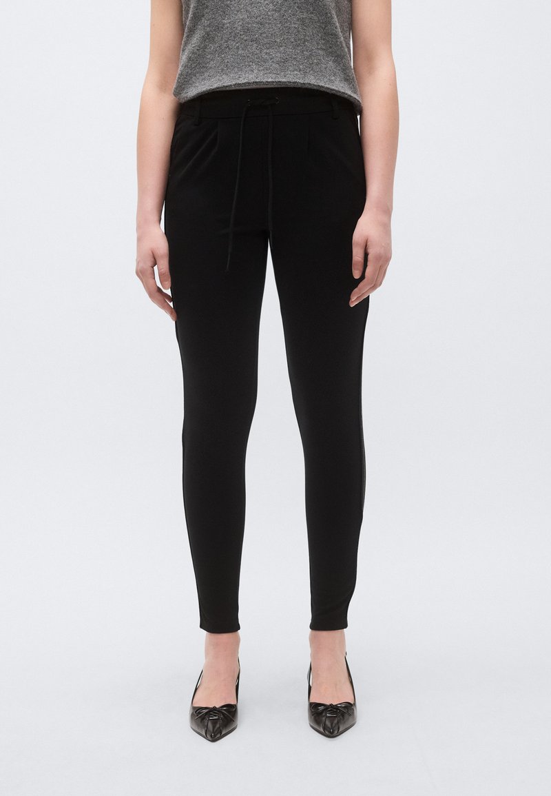 Pantaloni negri ajustați, cu talie cu șnur, buzunare laterale și textură fină, asortați cu pantofi negri cu vârf ascuțit.