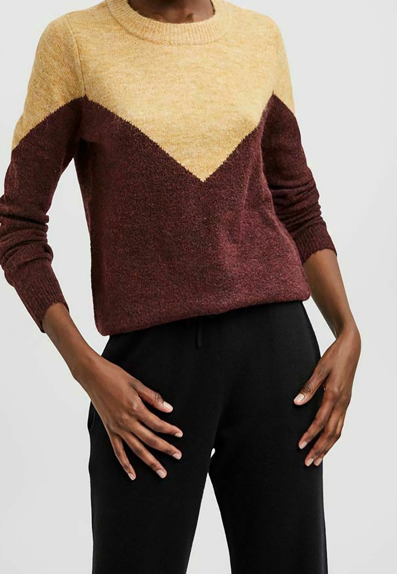 Maglione lavorato a maglia con motivo a zig zag giallo e bordeaux, colletto rotondo e polsini a coste, abbinato a pantaloni della tuta neri.