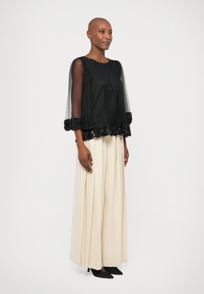 Black blouse with sheer tulle sleeves and floral lace trim. Paired with cream wide-leg pants and black pointed shoes.