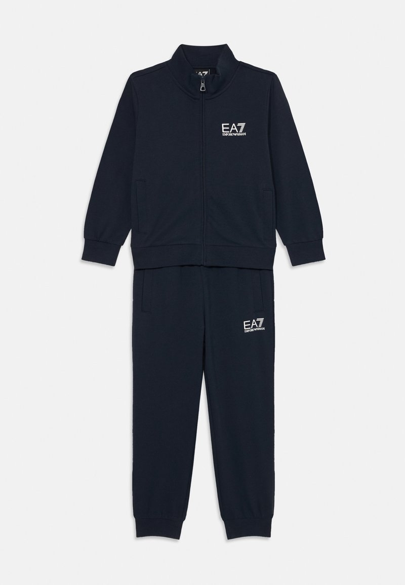 Tmavomodrý teplákový set s návrhom na zips a stojacím golierom, doplnený o zhodné nohavice s bočnými vreckami. Zmes bavlny.
