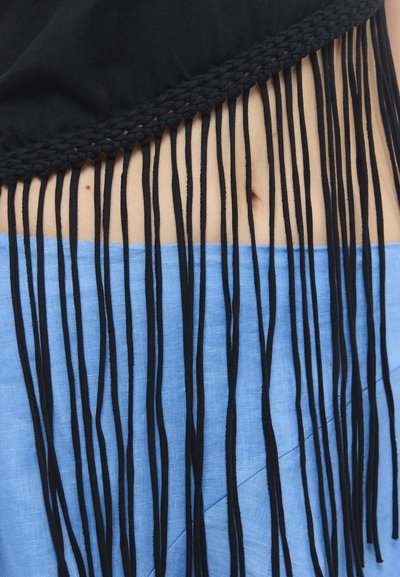 Fekete crop top, fonott szegéllyel és hosszú fekete bojtokkal, világoskék len szoknyával párosítva, amelynek ferde varrása van.