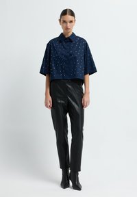 Camicetta blu navy a maniche corte con bottoni e borchie argentate; abbinata a pantaloni in pelle nera aderenti e stivaletti con punta a punta.