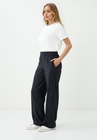 Schwarze weit geschnittene Hosen mit einem elastischen Bund und seitlichen Taschen, kombiniert mit einem taillierten weißen T-Shirt. Glatter Stoff, lässiges Design.