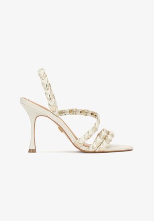 Højhælede sandaler i off-white med flettede remme, en spids tå og en stiletthæl. Har metallic accenter på remmene.