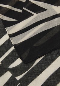Schwarz-weißer bedruckter Stoff mit transparenter Textur. Hat auffällige, unregelmäßige Streifen. Die Kanten sind gesäumt, was strukturierte Details hinzufügt.