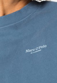 Sudadera de algodón azul oscuro con cuello redondo y un logo blanco impreso cerca del cuello, con detalles de textura acanalada.
