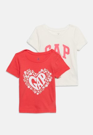 To børns T-shirts med korte ærmer, den ene rød med blomsterhjerte og teksten "GAP", den anden hvid med stor lyserød "GAP" tekst foran.