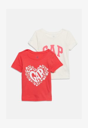 Deux t-shirts à manches courtes pour enfants, un rouge avec un cœur floral et le texte "GAP", un blanc avec un grand texte rose "GAP" sur le devant.