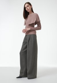 Hellrosa geripptes Sweatshirt mit einem geschichteten Design, kombiniert mit grauen, weit geschnittenen Hosen mit einem strukturierten Muster und Vorderfalten.