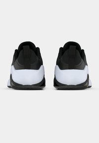 Crne atletske tenisice s reljefnim gornjim dijelom, bijelim potplatom i crnim detaljima; sadrže petnu traku i zakrivljeni oblik za stabilnost.