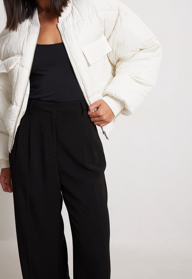 Doudoune blanche avec un col côtelé et une poche avant, associée à un pantalon noir taille haute à plis.