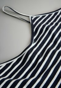 Mustvalge triibuline varrukateta särk õhukeste rihmadega, tasapinnal heleda halli pinnal.