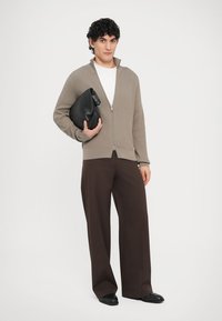 Φωτεινό μπεζ ριμπ πλεκτό ζακέτα με φερμουάρ, λευκό t-shirt από κάτω, σκούρο καφέ παντελόνι φαρδιάς γραμμής, κρατώντας μαύρο τσαντάκι χειρός. Απλός, μοντέρνος σχεδιασμός.