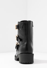 Černé kožené kotníkové boty s texturovaným povrchem, zdobené zlatými přezkami a akcenty, s nízkým zafalcovaným podpatkem a vzorkovanou podrážkou.