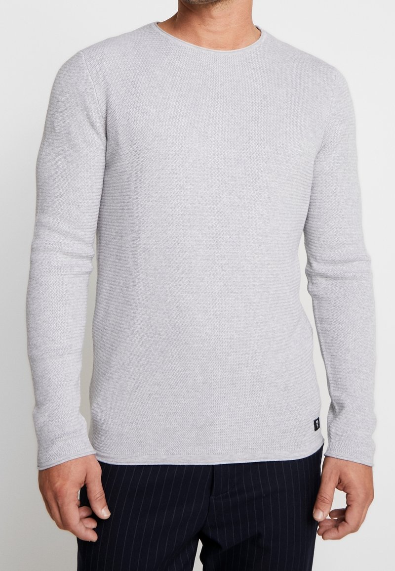 Ljusgrå, ribbad stickad långärmad tröja med rund halsringning och figurnära form, som har en liten logotag i kanten.