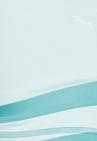 Un reggiseno sportivo di colore azzurro chiaro caratterizzato da un tessuto testurizzato, un design curvo e una striscia turchese a contrasto vicino all'orlo. Il logo Puma è visibile.