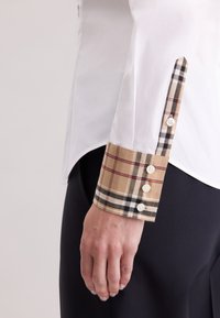 Weißes Hemd mit einer beige karierten Manschette, die schwarze und rote Linien aufweist. Die Manschette hat fünf weiße Knöpfe. Glatter Stoff und maßgeschneiderte Passform.