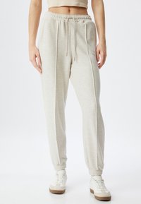 Lichtgrijze, hooggeplaatste joggers gemaakt van zachte stof, voorzien van een trekkoord in de taille, geribbelde boorden en verticale naaddetails.