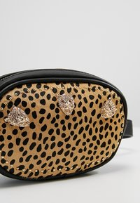 Torba w panterkę z złotymi ćwiekami i trzema metalicznymi akcentami w kształcie kociej twarzy. Czarna skórzana lamówka i zamek błyskawiczny. Okrągły kształt z regulowanym paskiem.