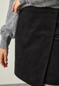 Black corduroy skirt with a side slit, textured fabric, and a smooth hem. A gray knitted sweater partially visible above the skirt.