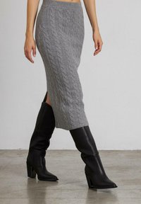 Grijze gebreide midi-skirt met kabelpatroon, voorzien van zijslits en een geribde tailleband. Gecombineerd met zwarte kniehoge laarzen met spitse neuzen.