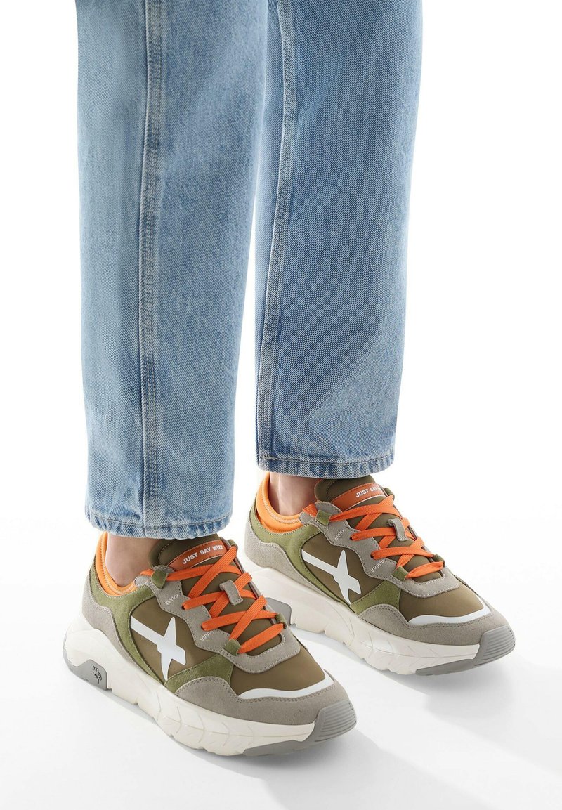 Gröna och grå sneakers med vita stjärnaccenter, orange snören och en texturerad sula, kombinerade med ljusblå tapered jeans.