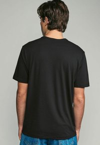 Camiseta de algodón negra con cuello redondo y mangas cortas, con una textura suave y un corte relajado, vista desde la parte de atrás.