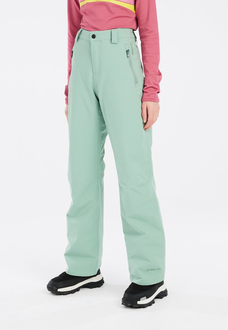Mintgroene skibroek met waterdicht materiaal, een tapered ontwerp, riemlussen en ritssluiting zijzakken. Zwarte wandelschoenen worden gedragen.