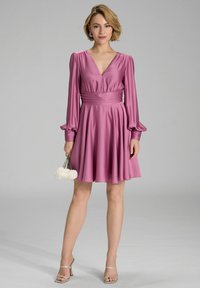 Pink satin dress with a deep V-neckline and long puffed sleeves. The waist is cinched, and the skirt flows to mid-thigh. Accessories include a small bouquet.