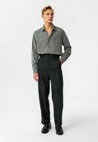 Grijze button-up shirt met een gladde textuur, gecombineerd met donkere gepinstrepen broeken en zwarte schoenen. Slim-fit silhouet, strakke lijnen.