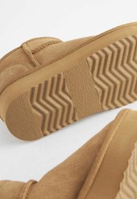 Tan ruskind ankle boots med en tekstureret gummisål. Sålen har et zigzag-mønster, der giver greb og stabilitet.