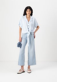 Blue and white striped short-sleeve shirt with a tie front, paired with light denim flared pants and beige slip-on shoes.