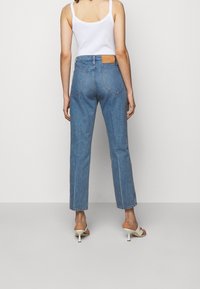 Jeans de mezclilla de tiro alto, de color azul claro, con piernas rectas, bolsillos traseros cosidos y una etiqueta de cuero color tostado en la cinturilla.