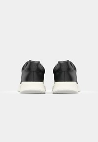 Černé kožené tenisky s elegantním designem, vybavené bílou podrážkou a polstrovaným límcem. Značka je ražena na patě.