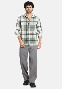 Camicia a quadri verde e bianca con accenti neri, abbinata a pantaloni grigi e scarpe chunky nere. Tessuto liscio, maniche lunghe arrotolate.