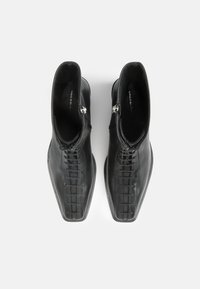 Černé kožené kotníkové boty s elegantním, strukturovaným designem, který zahrnuje texturované detaily a boční zip pro zapínání.